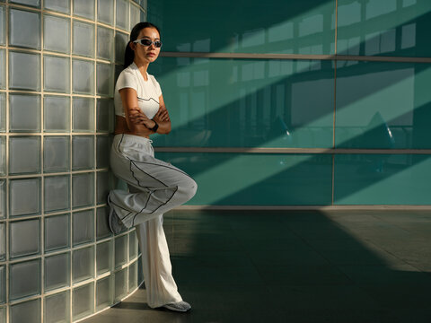 Confident woman leans against a glass wall in modern architecture