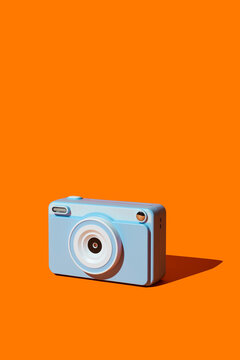 A blue instant camera sits on an orange background with a long shadow