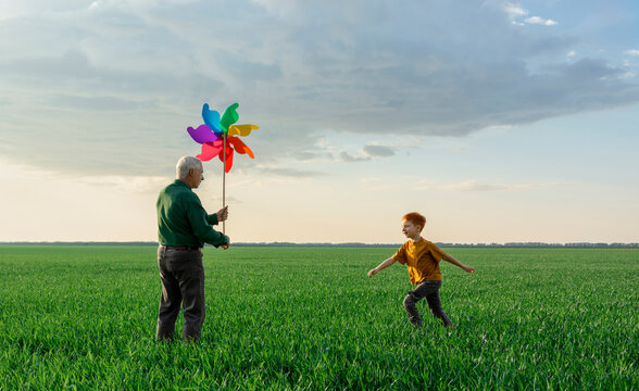 Grandson runs to his grandfather holding a pinwheel in a green field