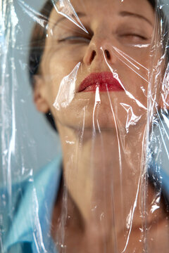 Mature woman standing behind a plastic film depicting suffocation