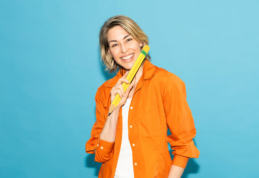 Smiling woman in orange shirt holds large paper pencil for drafting