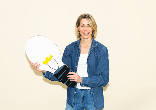Smiling woman holds a paper lightbulb indoors showing creativity