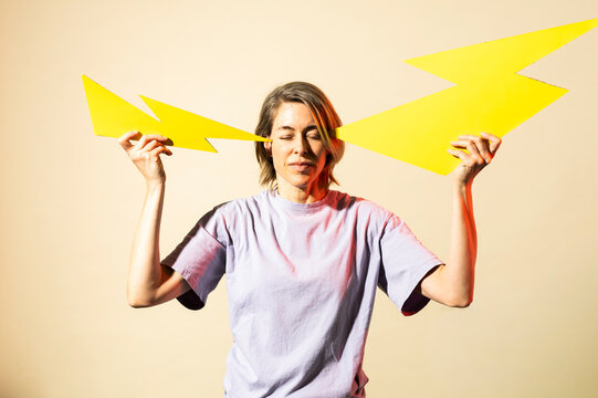 Woman holds paper lightning to head indoors experiencing headache