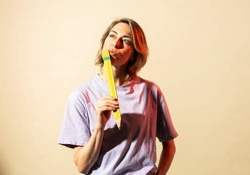 Woman holding large pencil while thinking about creative ideas