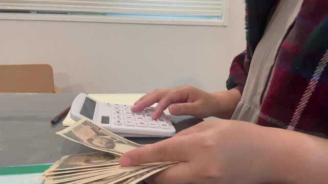電卓を使いながら計算して家計簿をつける女性