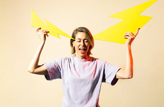 Woman holds yellow paper lightning to her head in pain
