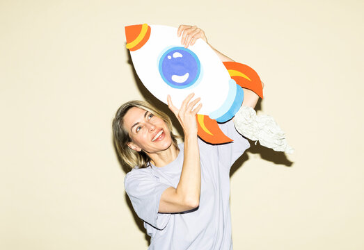Smiling woman holds a handmade paper rocket indoors