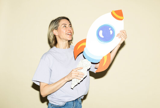 Smiling woman holds a paper rocket indoors for business growth