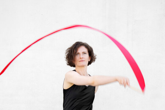 Joyful woman in black dress twirls a red ribbon indoors