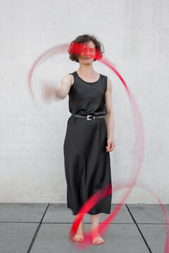 A barefoot woman in a black dress spins a red ribbon outdoors
