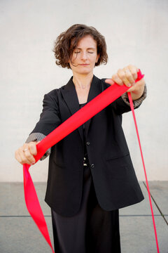 Calm woman in a black blazer holds a red ribbon outdoors