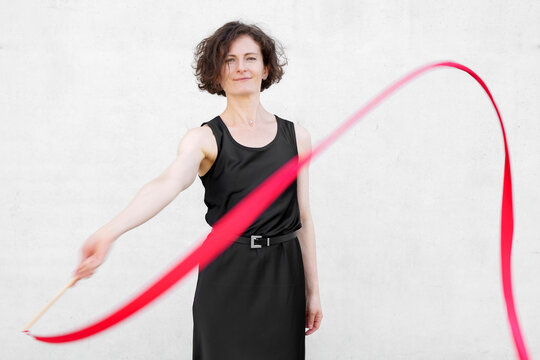 Woman in black dress dancing with a red ribbon against white wall