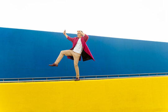 Man taking a selfie while balancing on a yellow wall