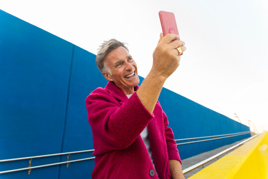 Man in fuchsia coat takes selfie with smartphone