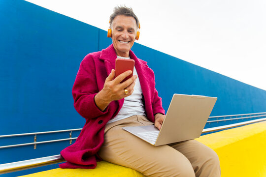 Man sitting outdoors using smartphone and laptop
