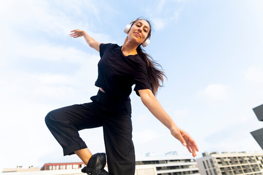 Woman in black clothing dances with headphones outdoors in the city