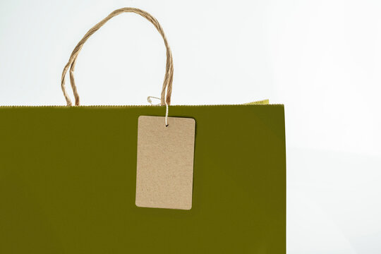 Close-up of an olive green paper shopping bag with a twisted handle and a blank brown kraft paper tag on a white background, perfect for retail mockup designs. Template for copy space or mockup