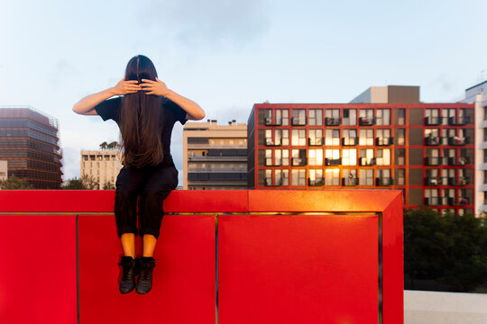 Female dancer sits on a red urban wall with hair covering her face