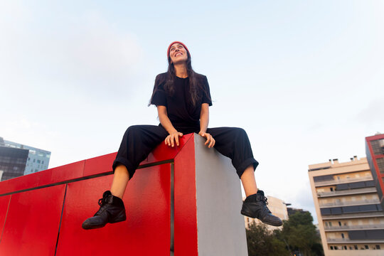 Confident female dancer sits on a red wall in urban Barcelona