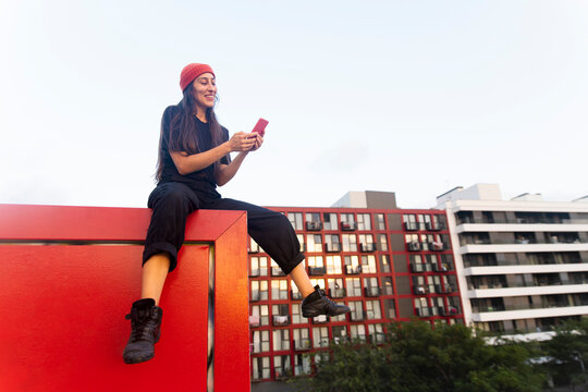 Woman sitting on a red wall using a smartphone in the city