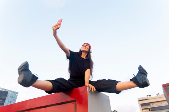 Smiling female dancer takes a selfie while doing a split outdoors
