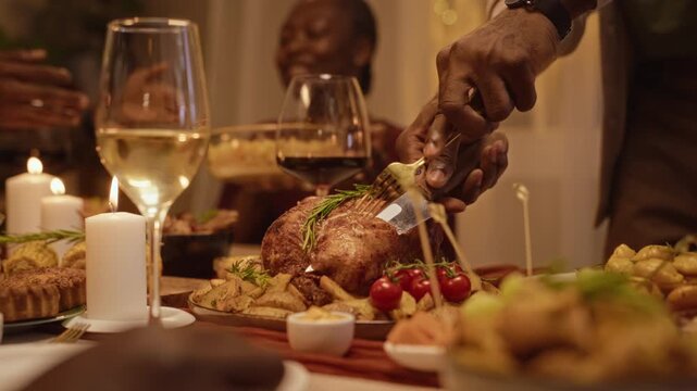 African American man carving roasted turkey at festive dinner table with friends. Footage useful for Thanksgiving advertising, holiday food commercials and restaurant marketing