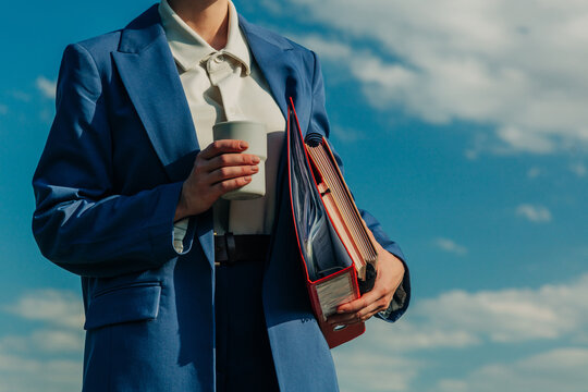 Businesswoman in blue suit holds coffee and folders outdoors