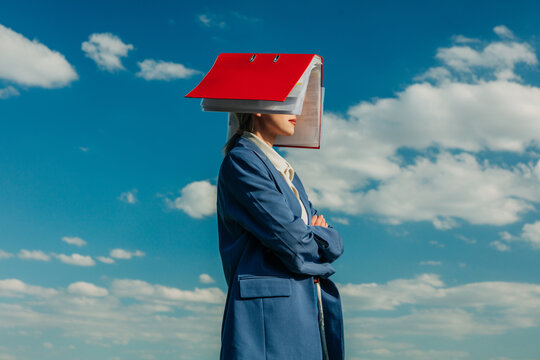 Businesswoman hides face under red folder against blue sky