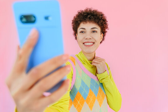 Smiling woman taking a selfie with phone against pink background