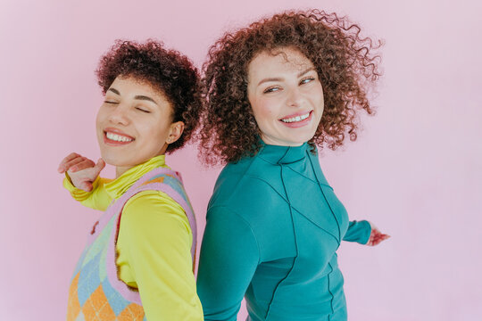 Smiling friends dancing and having fun in colorful fashion against pink