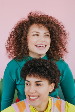 Smiling friends with curly hair in front of a pink background
