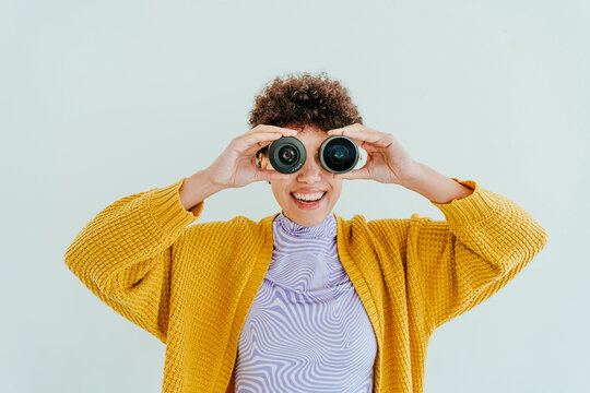 Smiling woman in orange sweater looking through binoculars indoors