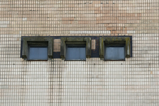 Three rectangular windows set into a beige tiled building facade