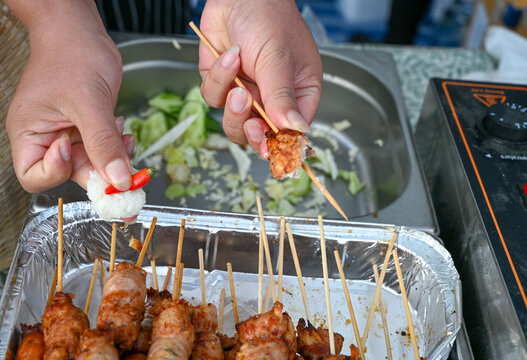 A woman offering traditional Thai food. Grilled pork skewers. Vendor selling Nem lụi, popular Southeast Asian street food skewers. Hands of woman holding  food. 