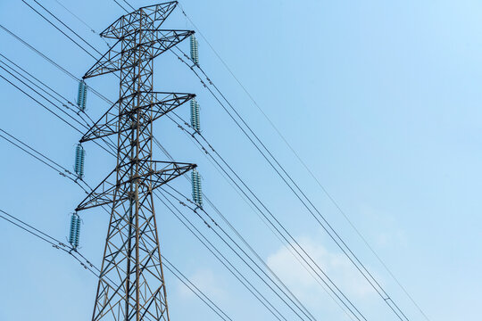 High-voltage electricity transmission tower with power lines and glass insulators against a clear blue sky. Concept of the electricity energy industry