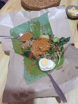 Traditional Indonesian pecel salad made of boiled vegetables served with peanut sauce on banana leaf.