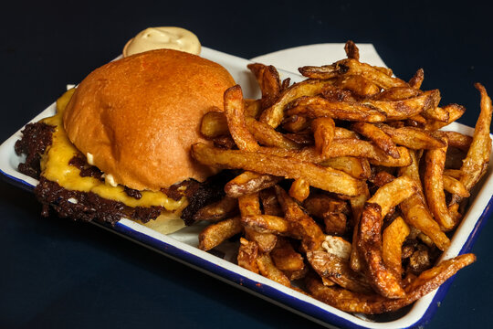 Gourmet cheeseburger with melted cheese, crispy fries and creamy sauce served on a rustic enamel tray.