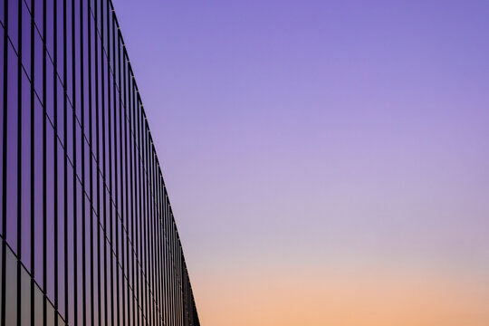 A minimalist architectural view of a modern glass building facade with geometric lines against a colorful purple and orange sunset sky.concept building business