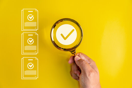 Hand using a magnifying glass to verify documents, checklists and quality standards, symbolizing compliance, approval, inspection, validation and careful business process review