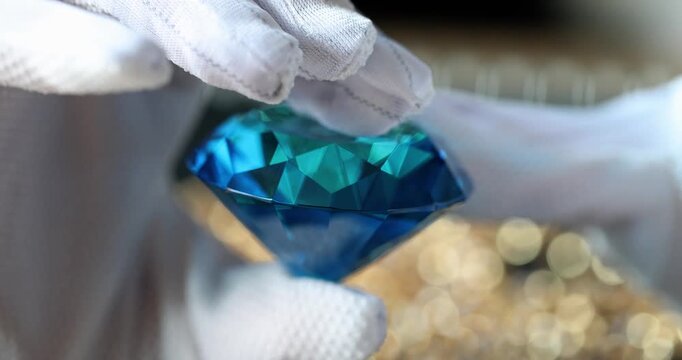 Glistening under soft golden lights, a delicate hand lifts a stunning blue diamond with care. This moment captures the elegance and beauty of this precious gem, revealing its facets.