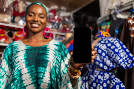 African woman small business owner showing a blank smartphone screen in her clothing store