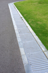 Obraz premium Long metal drainage grate along the curved edge of a road and lawn.