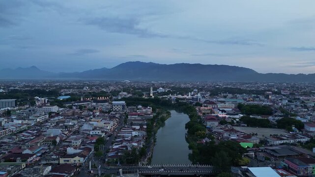 Banda Aceh, Indonesia : Backward aerial drone footage of riverside mosque and residential area in Banda Aceh of Sumatera, Indonesia toward Baiturrahman Grand Mosque and mountain under sunset sky