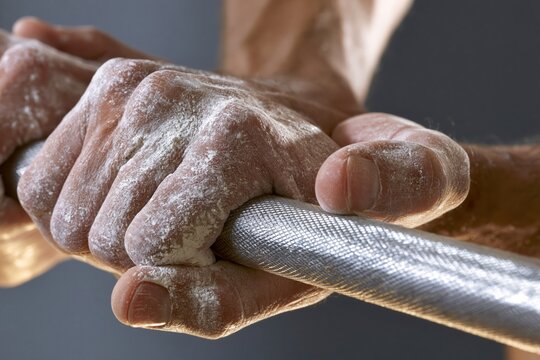 Close detail of hands gripping knurled bar with chalked skin
