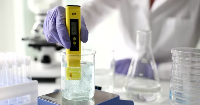 A scientist in a lab carefully measures the pH of a liquid sample with a digital meter. The bright yellow device contrasts with the clear beaker, showcasing precision in research.