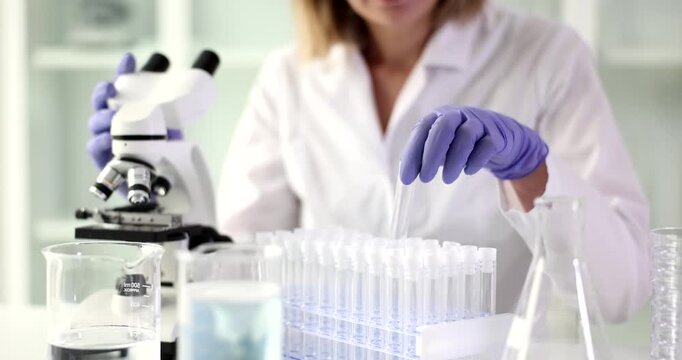 In a busy laboratory, a dedicated scientist examines samples under a microscope, preparing test tubes for detailed analysis and discovery. Focused and precise, the work unfolds.
