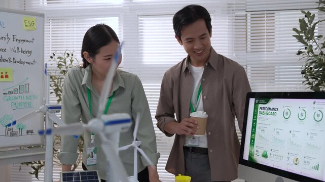 ESG Meeting Report with Asian Colleagues Reviewing Sustainability Planning, Renewable Energy Data, Solar Panel Prototype, Model House, and Environmental Strategy in Modern Office Setting with Plants