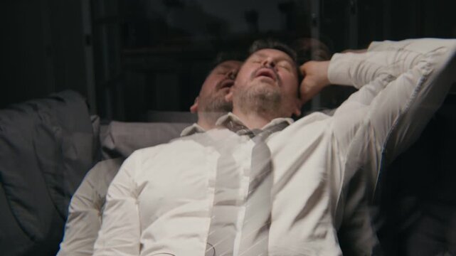 Middle aged Caucasian businessman drinking alcohol with double vision effect, collapsing exhausted on sofa. Clip suitable for substance abuse campaigns and corporate burnout awareness