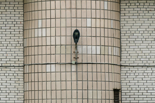 Curved beige-tiled column features black wall-mounted light fixture against white brick facade