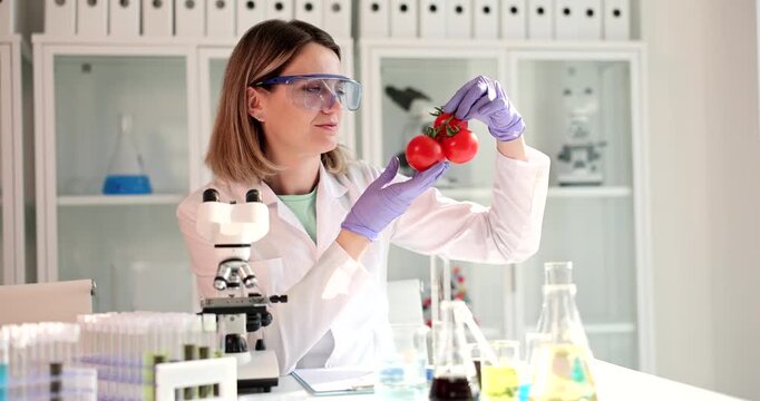 A researcher examines bright red strawberries in a lab filled with glass containers and scientific equipment. She carefully inspects each berry for quality and insights.